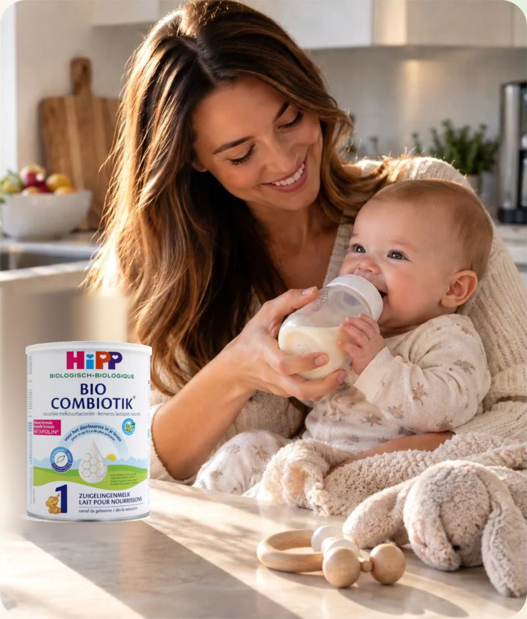 Mother bottle-feeding her baby in a bright kitchen beside a tin of HiPP Bio Combiotik Stage 1 organic European baby formula
